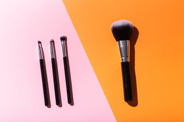 Various make-up brushes on pink and orange background, top view. Cosmetics and beauty concept.