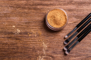 Loose compact mineral powder for face and a brushes for powder and visage on wooden background with copy space. Eco friendly and organic cosmetics.