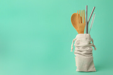 Bag with bamboo cutlery, metal straws and brush on turquoise background, space for text. Conscious...