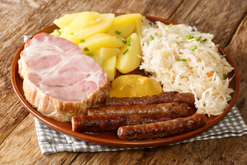 Smoked pork neck and sausages with cabbage Sauerkraut boiled potatoes and mustard closeup in the plate on the table. Horizontal