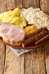 smoked Kassler pork neck and fried sausages with Sauerkraut mashed potatoes and mustard on wooden table closeup in the plate on the table. Vertical