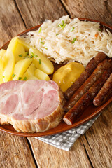 Kassler and sausages served with sauerkraut and boiled potatoes closeup in the plate on the table. Vertical
