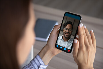 Close up view of young woman hold use cellphone talk speak on video call with African American man. Biracial multiethnic people have webcam digital virtual communication on smartphone device.