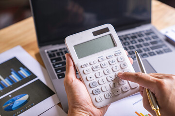 Accountant or banker working process, a Businesswoman using a calculator to calculate the numbers of statistic business profits growth rate on documents graph data, his desk in an office. - obrazy, fototapety, plakaty
