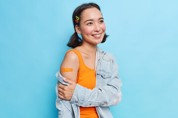 Pleased teenage girl with eastern appearance has two pony tails smiles gently happy to get vaccine...