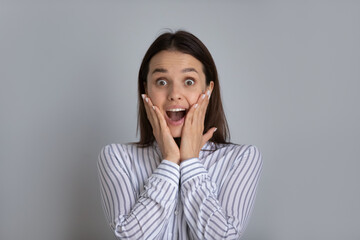 Portrait of happy excited millennial Caucasian woman isolated on grey studio background surprised by good sale offer or promotion discount or deal. Overjoyed young female shocked by unexpected news.