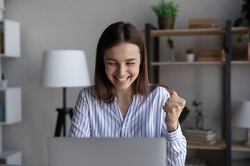 Smiling millennial Caucasian woman look at laptop screen triumph win online lottery on gadget....