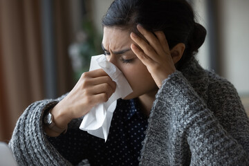 Unhealthy young Indian woman covered in blanket blow nose suffer from flu or cold. Unwell...