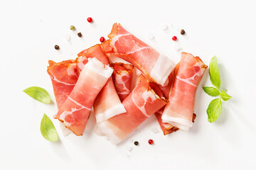 Tasty prosciutto slices with basil leaves and spices on white background