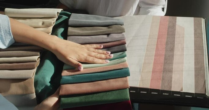 A woman buyer picks up textiles in the store, compares the shade with the catalog of wallpaper. The seller holds an album with samples