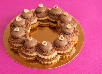 Cake with round biscuits, brown cream, brown macaron and nuts on golden plate and pink background