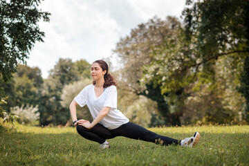 Fototapeta premium Warmup at the park. A young fit woman in sports clothes doing stretching. The concept of wellness