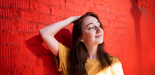 Fototapeta premium Beautiful young happy brunette woman with a smile in a yellow t-shirt on a background of a red brick wall