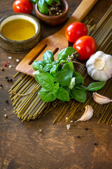 Ingredients for italy cuisine. Spinach spaghetti, herbs, spices, olive oil and tomatoes on a rustic table. Copy space.
