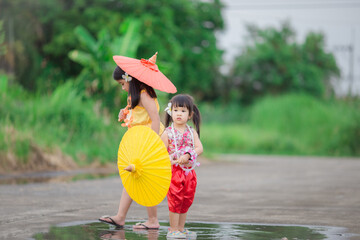 Close-up background view of two young Asian girls running or teasing in blur on the street in front of the house, doing activities together outside the classroom during the holidays.