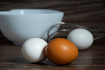 Whisk eggs. White and orange eggs lie on the table near the bowl.
