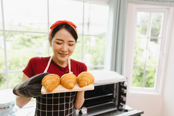 Young smiling asian female baking Croissant in oven, Bakery cooking concept with copy space