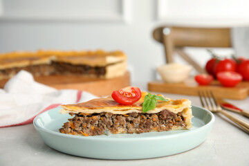 Piece of delicious pie with minced meat, tomato and basil served on light marble table, closeup