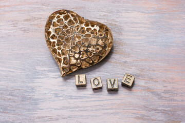 Heart shaped gold color metal and a word LOVE on a surface with faded paint