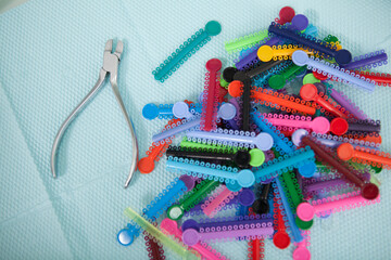 Close up of many colorful braces elastic bands and dentists instrument on blue background