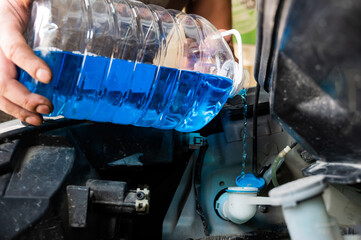 Auto mechanic pours windshield washer fluid into the car.