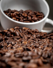 Beans of roasted coffee poured out of the white cup on the table. Morning. Cheerfulness. Close-up