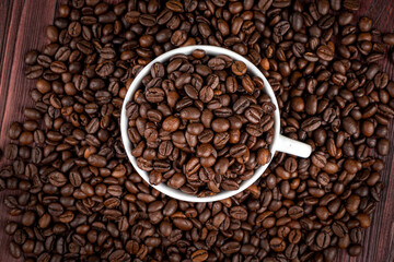 Scattered on the table beans of roasted coffee in a white cup. Morning. Cheerfulness