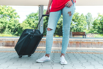 Body part and suitcase. A woman with a suitcase is waiting at the station.