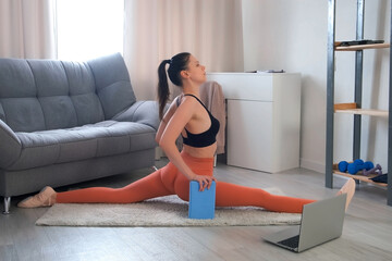 Flexible sporty young woman making longitudinal split sitting on carpet. Online home fitness, yoga,...