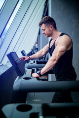 Fototapeta na wymiar Sporty strong man training cardio in the gym. Male runner on treadmill in gym doing cardio workout.