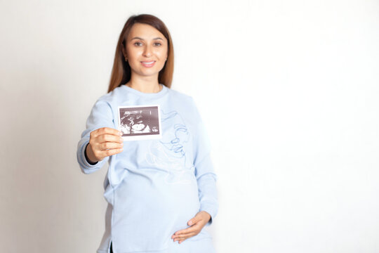A beautiful pregnant woman with dark hair holds an ultrasound image of the child. screening. Pregnancy monitoring. White background, space for text