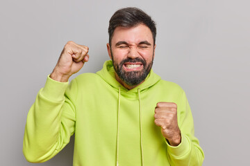 Happy bearded man clenches fist from happiness rejoices something feels like winner clenches teeth...