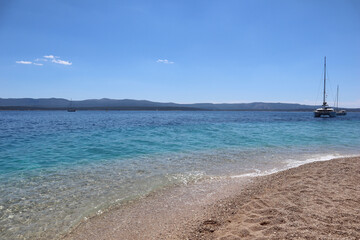 Fototapeta na wymiar Seascape yacht by the coast on the Zlatni Rat beach with clear turquoise water on a sunny summer day, Croatia