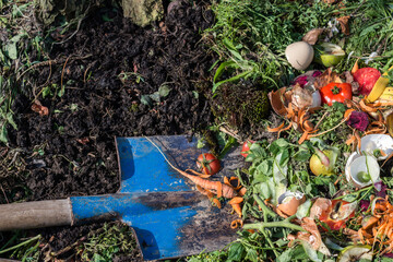 Compost box outdoors full with garden browns and greens and food  wastes, blue shovel in the soil,...
