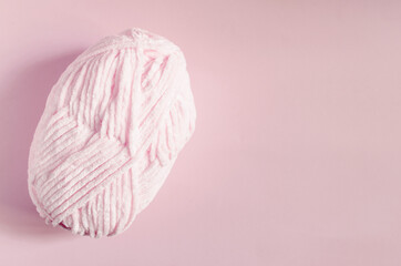 A skein of light pink yarn on a pink background top view is a place for text. An object for creativity and knitting a ball of pink thread