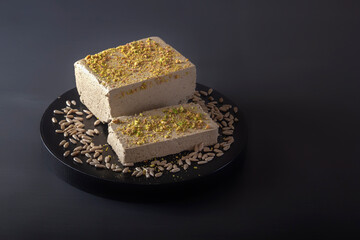 Sunflower halva sprinkled with crushed nuts and pistachios on a black plate on a dark background. Close-up