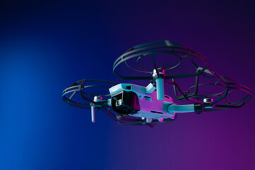 a small unmanned aerial vehicle with the protection of the propeller blades in flight on a neon background inside the room