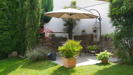Sitzplatz in einer Gartenecke mit Tisch und Stühlen unter einem Sonnenschirm