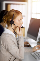 Friendly caucasian businesswoman talking by headset in sunny office. Call center and diverse people group in business