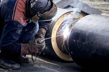 Construction worker arc welding the metal pipe.