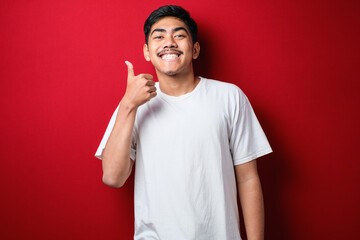 Fat Asian guy wearing a white t-shirt smiles at the camera while showing his thumbs up. - obrazy, fototapety, plakaty