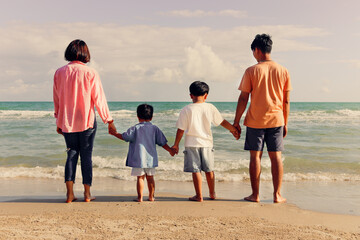 Happy family four spend time and have fun together on summer holiday vacation, cheerful parents children hold hands from behind on tropical sea beach, resting and relaxing weekend on beach.