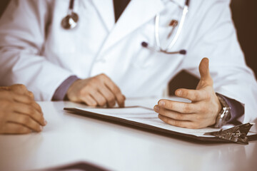 Unknown male doctor and patient woman discussing something while sitting in clinic. Best medical service in hospital, medicine, pandemic stop