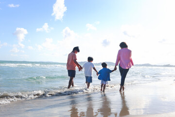 Happy family of four spend time together on summer holiday vacation, parents and children holding hand and walking along tropical sea beach, mother father and kids resting and relaxing on weekend