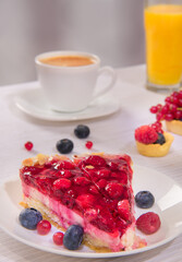 Raspberry cake on white plate multiple fresh berries on table glass of orange juice and white cup of coffee