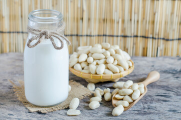 Closed up organic peanut milk in glass bottle with some peanut seed in wooden basket and spoon on grunge background