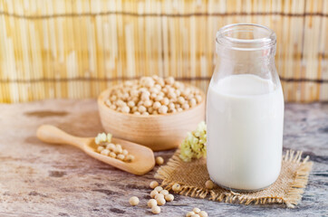 Closed up fresh organic homemade soybean milk in glass bottle over blur soybean seed pile in wooden bowl and spoon on grunge background in soft light tone