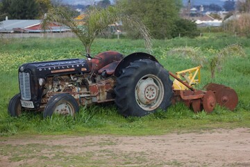 Obraz premium A tractor parked in the grass with cultivating machine attached to the back for farming purposes. 