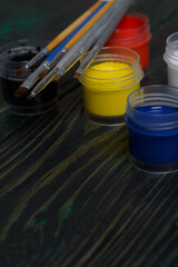 Gouache set for school. Tins of paint lie on pine boards. Nearby are paint brushes.