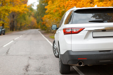 Fototapeta na wymiar Stylish white SUV car in autumn forest. 7 seats car for traveling with company. Colorful maple leaves and road on background. Traveller lifestyle and freedom concept. Rear view. Adventure in vacation.